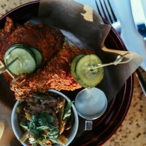 Tantalizing close-up of fried chicken topped with pickles served with a fresh side salad and dressing.