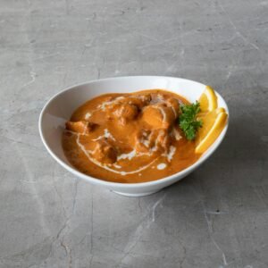 A savory bowl of butter chicken garnished with fresh herbs and citrus slices.
